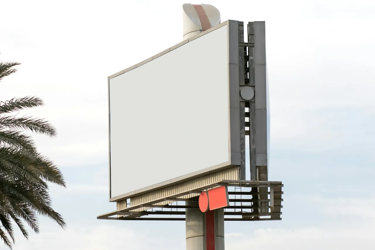 A blank roadside billboard against the sky, palm fronds to one side